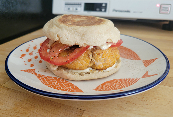 a light orange burger with tomato slices on an english muffin